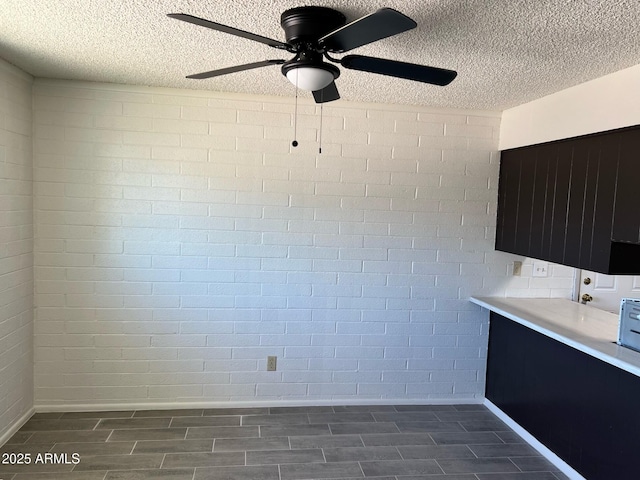 unfurnished dining area featuring baseboards, a ceiling fan, a textured ceiling, and wood tiled floor