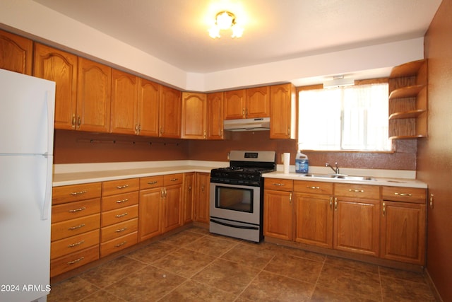 kitchen with dark tile patterned flooring, stainless steel gas range, sink, and white fridge