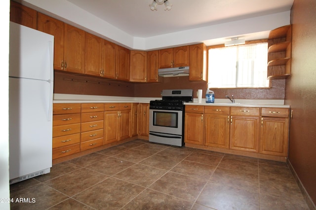 kitchen with white refrigerator, sink, dark tile patterned floors, and stainless steel range with gas stovetop