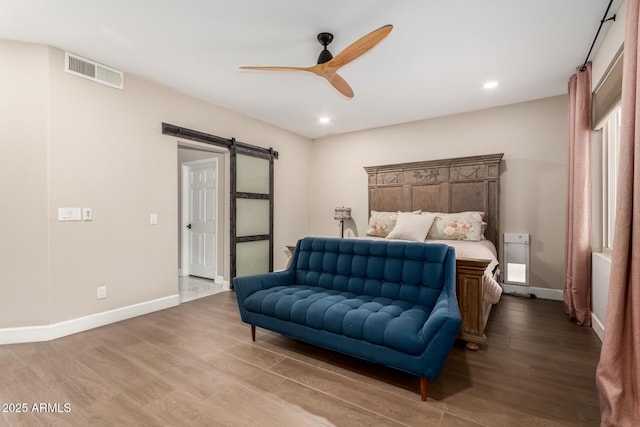 bedroom with ceiling fan, wood-type flooring, and a barn door