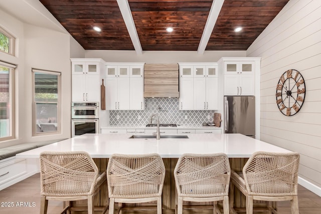 kitchen with wooden ceiling, appliances with stainless steel finishes, and a large island with sink