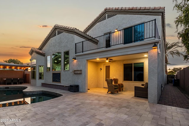 back house at dusk featuring a fenced in pool, ceiling fan, an outdoor living space, a patio area, and a balcony