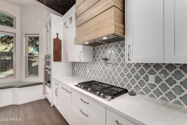 kitchen with premium range hood, white cabinetry, stainless steel appliances, and decorative backsplash