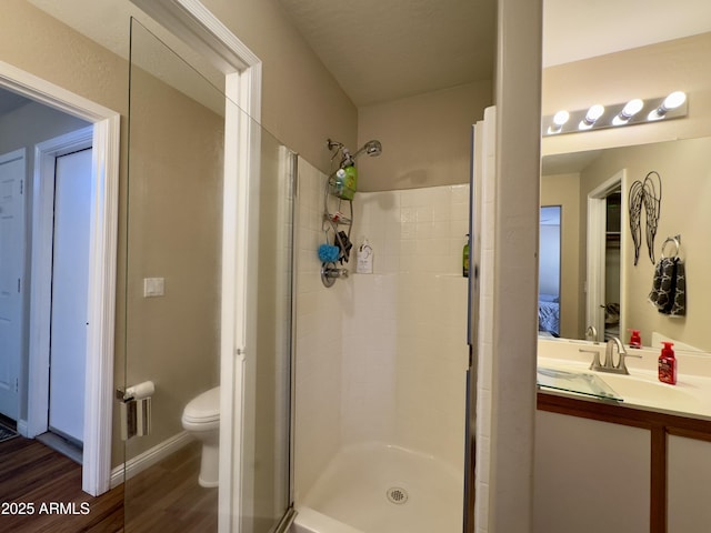 bathroom with toilet, wood finished floors, vanity, and a stall shower