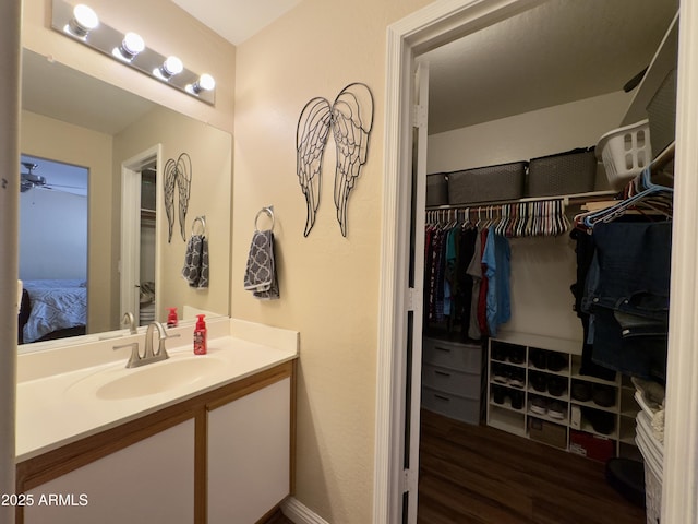 bathroom with wood finished floors, a spacious closet, vanity, ceiling fan, and ensuite bath