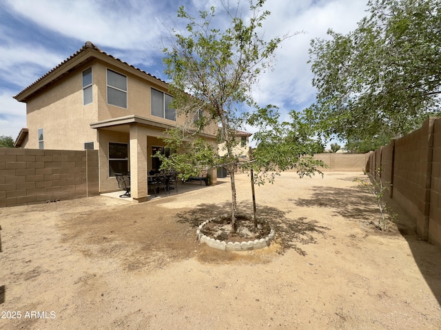 rear view of house with stucco siding, a fenced backyard, and a patio