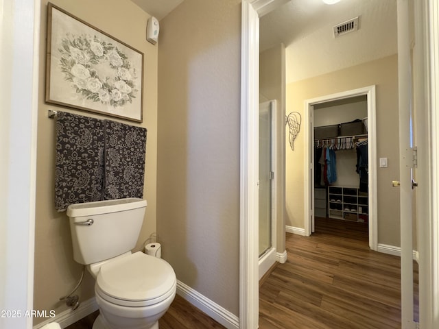 bathroom with a shower stall, wood finished floors, toilet, and baseboards
