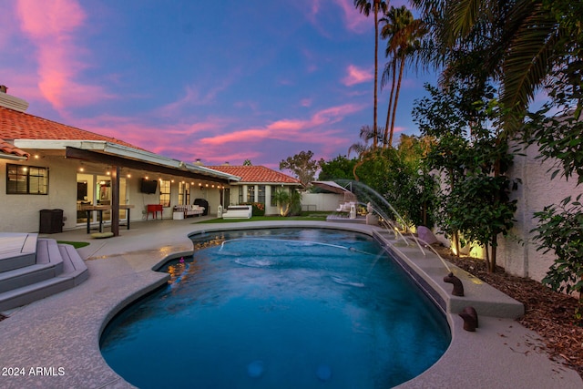 pool at dusk featuring pool water feature and a patio area