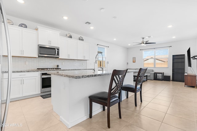 kitchen with light stone counters, appliances with stainless steel finishes, an island with sink, and white cabinets