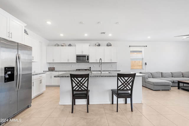 kitchen featuring a breakfast bar area, stainless steel appliances, dark stone countertops, a center island with sink, and white cabinetry