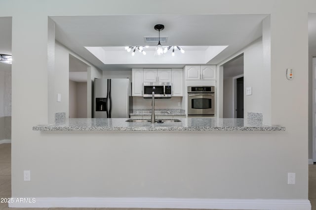 kitchen with sink, appliances with stainless steel finishes, a tray ceiling, light stone countertops, and white cabinets