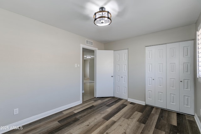 unfurnished bedroom featuring multiple closets and dark hardwood / wood-style floors