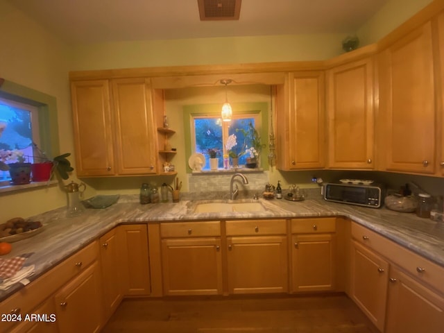 kitchen featuring light brown cabinetry, sink, decorative light fixtures, and light stone counters