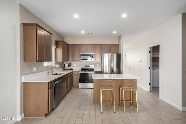 kitchen featuring a kitchen island, appliances with stainless steel finishes, a kitchen bar, light hardwood / wood-style flooring, and sink