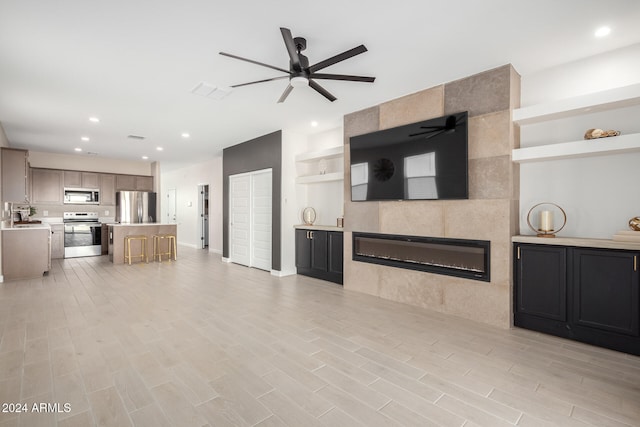 unfurnished living room featuring sink, a tiled fireplace, light hardwood / wood-style floors, and ceiling fan