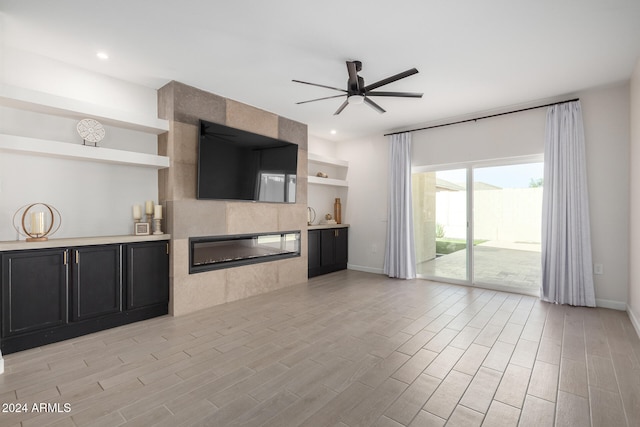 unfurnished living room featuring a tiled fireplace, ceiling fan, and light wood-type flooring