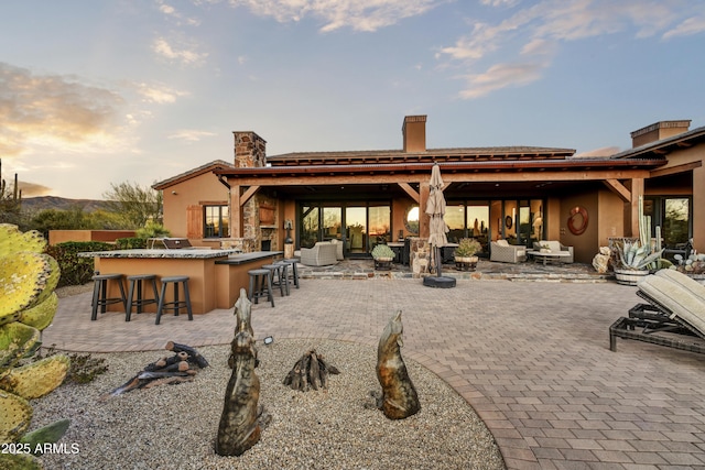 back house at dusk featuring an outdoor hangout area, a patio area, and an outdoor bar