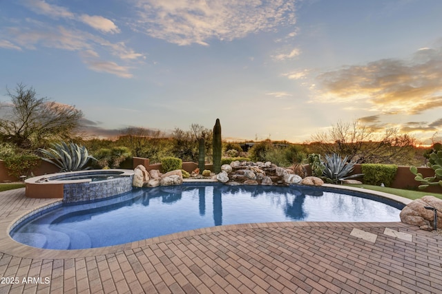 pool at dusk featuring an in ground hot tub