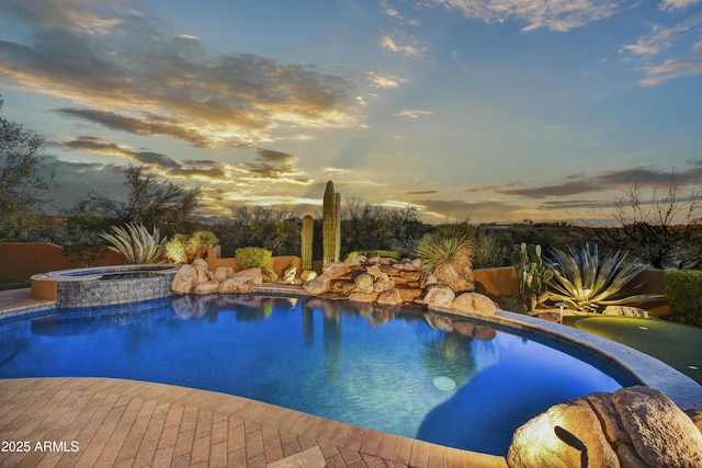 pool at dusk featuring an in ground hot tub