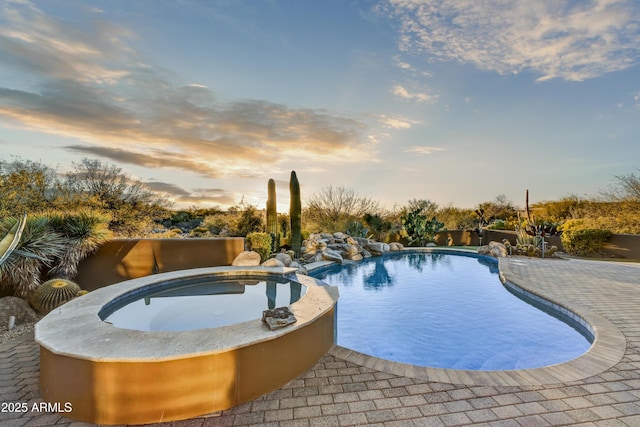 pool at dusk with an in ground hot tub