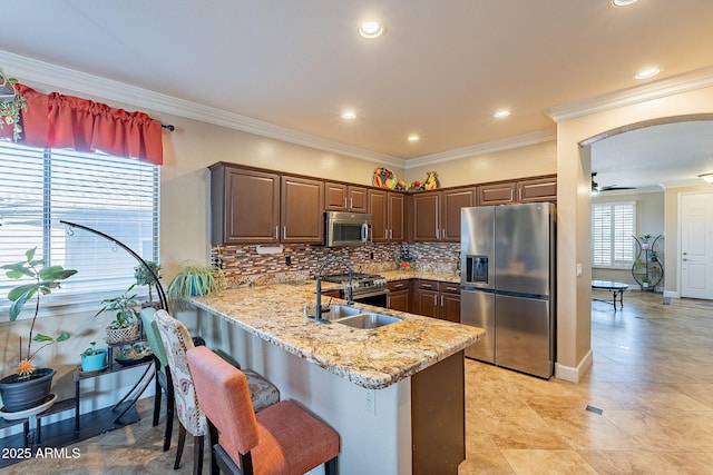 kitchen featuring appliances with stainless steel finishes, dark brown cabinetry, light stone countertops, decorative backsplash, and kitchen peninsula