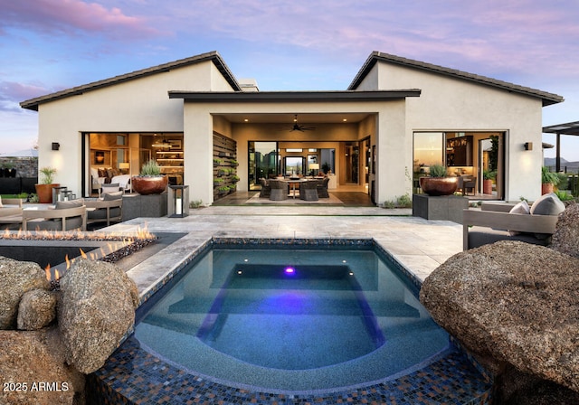 back house at dusk with outdoor lounge area, ceiling fan, a patio, and a hot tub