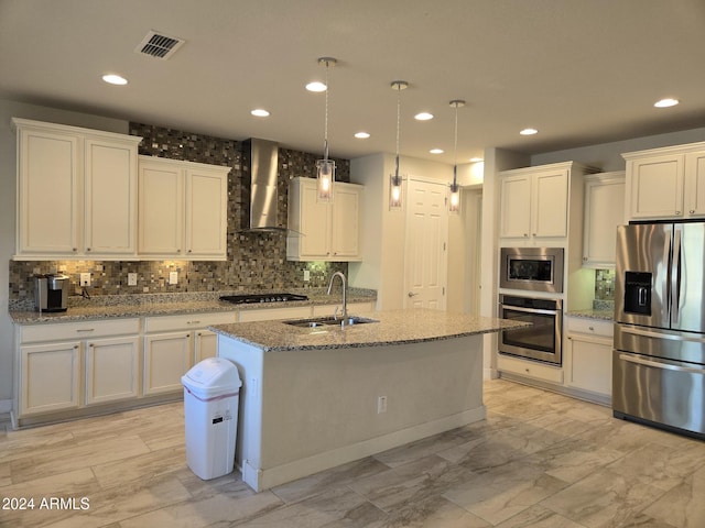 kitchen featuring stainless steel appliances, wall chimney range hood, white cabinetry, and a kitchen island with sink