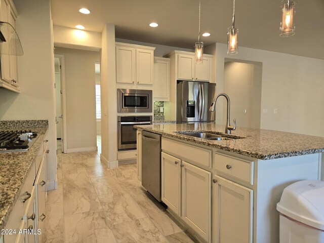 kitchen featuring light stone counters, sink, a kitchen island with sink, appliances with stainless steel finishes, and decorative light fixtures