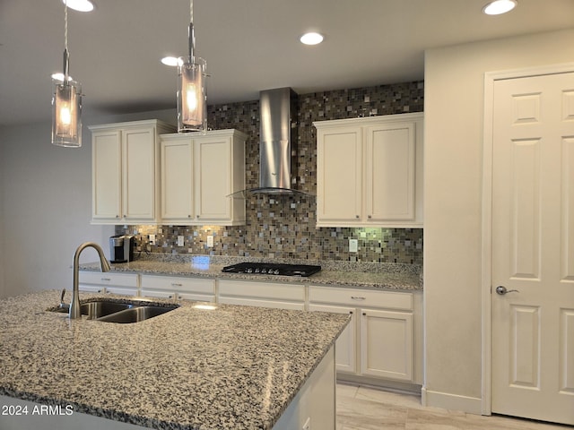 kitchen featuring white cabinets, sink, an island with sink, wall chimney range hood, and pendant lighting