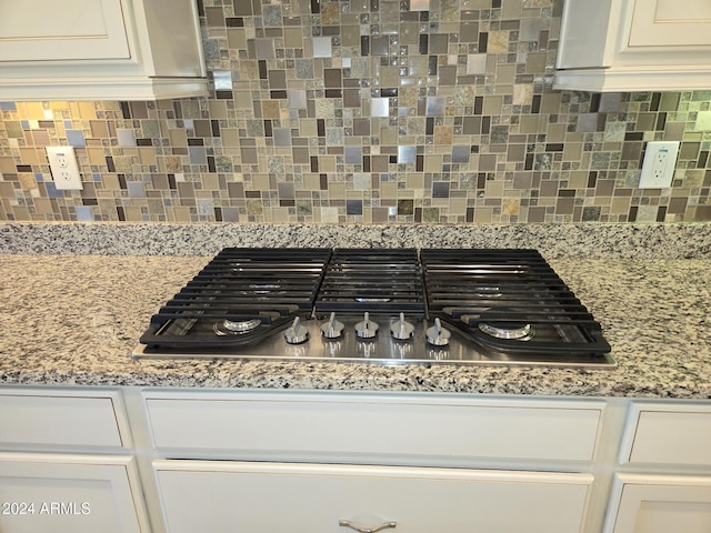 interior details featuring white cabinetry, stainless steel gas cooktop, light stone counters, and backsplash