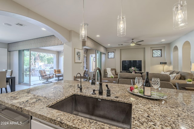 kitchen with hanging light fixtures, sink, light stone counters, and ceiling fan