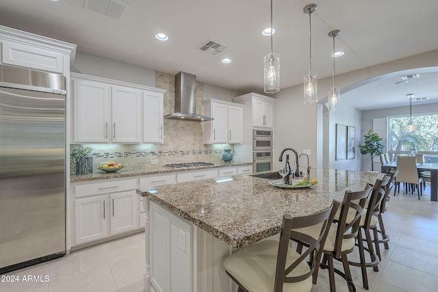 kitchen featuring appliances with stainless steel finishes, pendant lighting, wall chimney range hood, and white cabinets