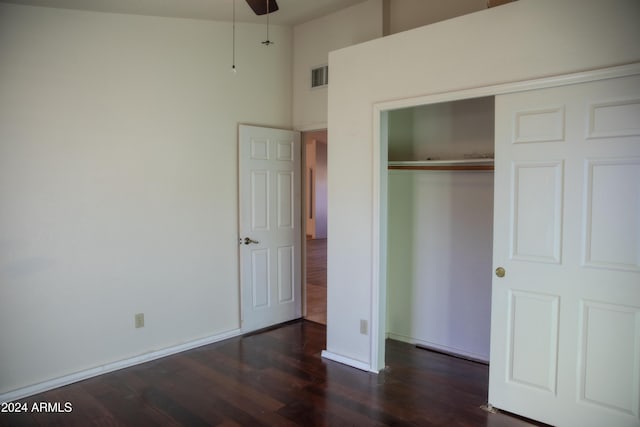 unfurnished bedroom featuring a towering ceiling, dark hardwood / wood-style floors, a closet, and ceiling fan