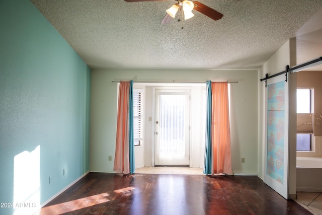 interior space with ceiling fan, a barn door, a textured ceiling, and dark wood-type flooring