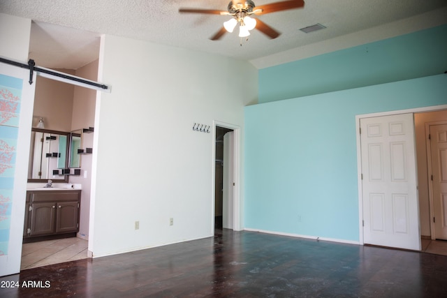 empty room featuring ceiling fan, sink, a barn door, a textured ceiling, and vaulted ceiling