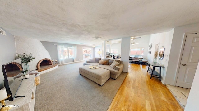 living area with light colored carpet, visible vents, a ceiling fan, a brick fireplace, and a textured ceiling