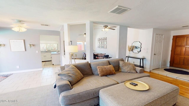 living area with light tile patterned floors, baseboards, visible vents, a ceiling fan, and a textured ceiling