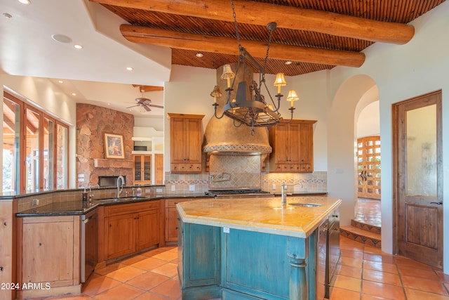 kitchen featuring beamed ceiling, light tile floors, sink, a center island with sink, and tasteful backsplash