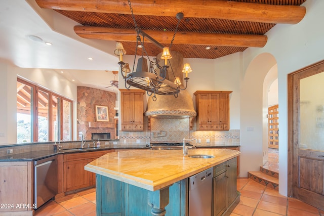 kitchen featuring backsplash, a kitchen island with sink, light tile floors, and beam ceiling