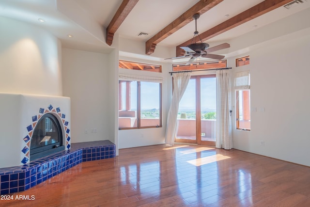 unfurnished living room featuring wood-type flooring, ceiling fan, a fireplace, and beam ceiling