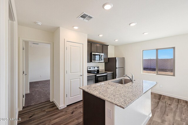 kitchen featuring visible vents, light stone counters, a kitchen island with sink, stainless steel appliances, and a sink