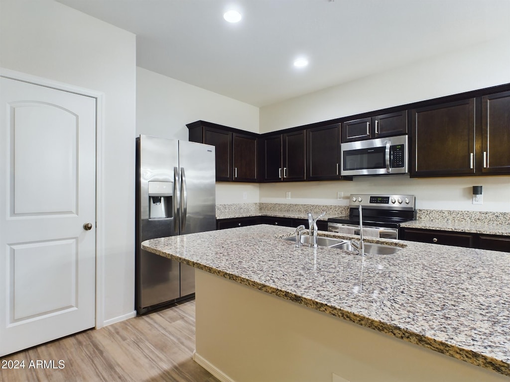 kitchen with dark brown cabinetry, light stone counters, light hardwood / wood-style flooring, and stainless steel appliances