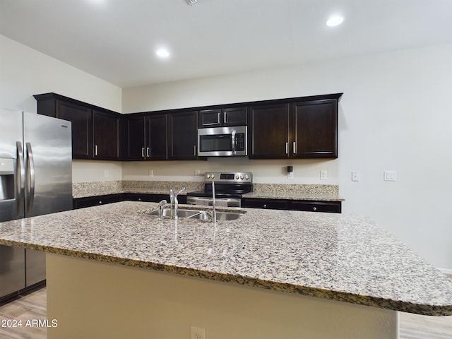 kitchen featuring appliances with stainless steel finishes, light wood-type flooring, light stone counters, a kitchen island with sink, and sink