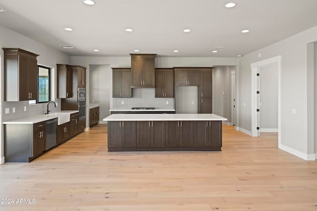 kitchen with backsplash, appliances with stainless steel finishes, a center island, and light wood-type flooring