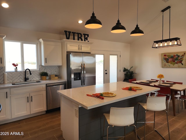 kitchen with stainless steel appliances, sink, hanging light fixtures, white cabinets, and a center island