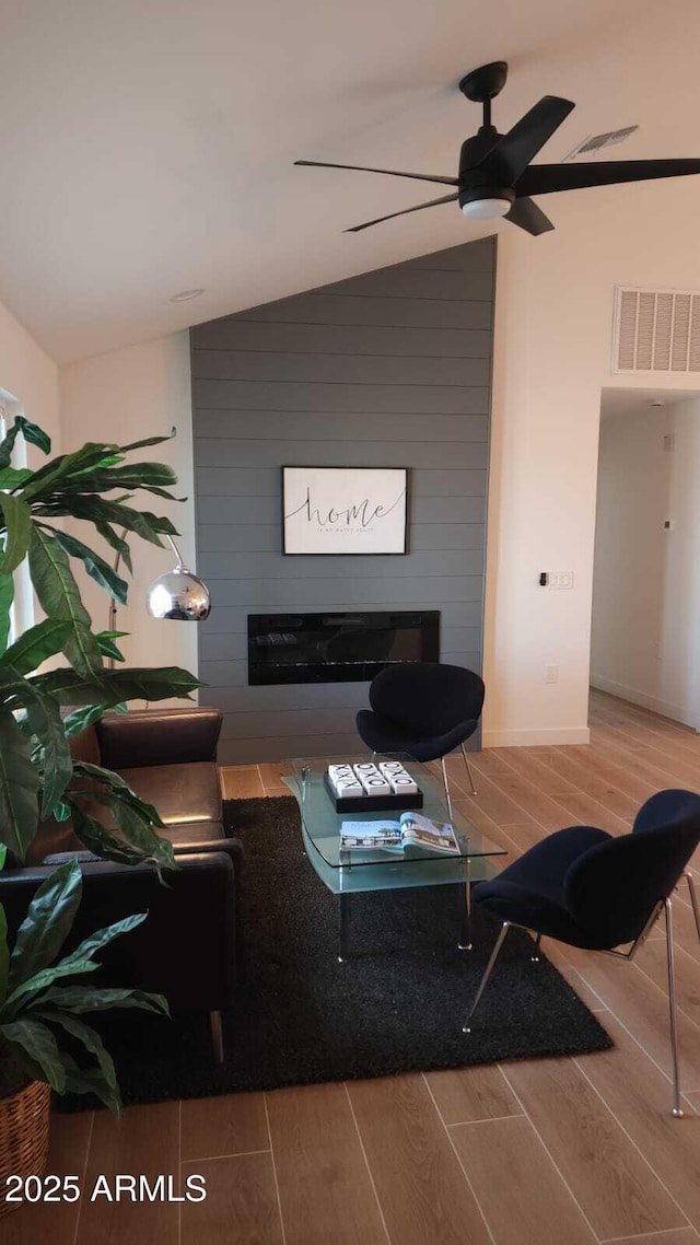 living room with vaulted ceiling, a large fireplace, and hardwood / wood-style flooring