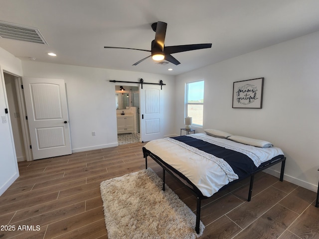 bedroom featuring ceiling fan, connected bathroom, and a barn door