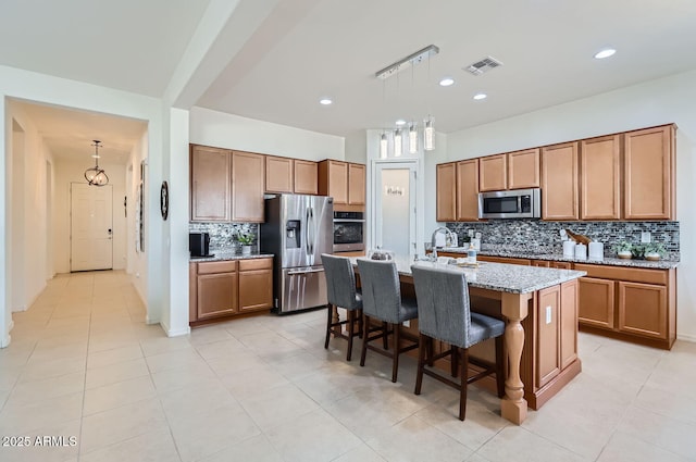 kitchen with a breakfast bar area, light stone counters, hanging light fixtures, a center island with sink, and appliances with stainless steel finishes