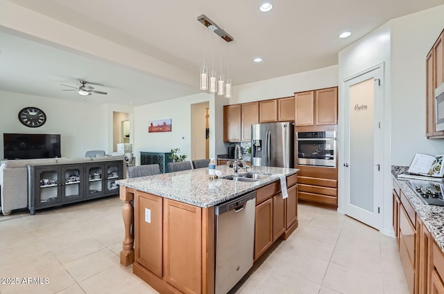 kitchen with ceiling fan, a kitchen island with sink, stainless steel appliances, light stone countertops, and decorative light fixtures