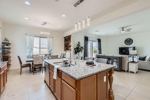 kitchen with sink, decorative light fixtures, light stone countertops, and a kitchen island with sink